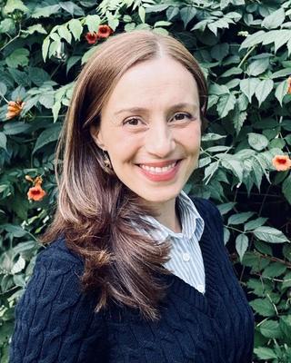 "Portrait of a smiling woman in front of leafy greenery with orange flowers.